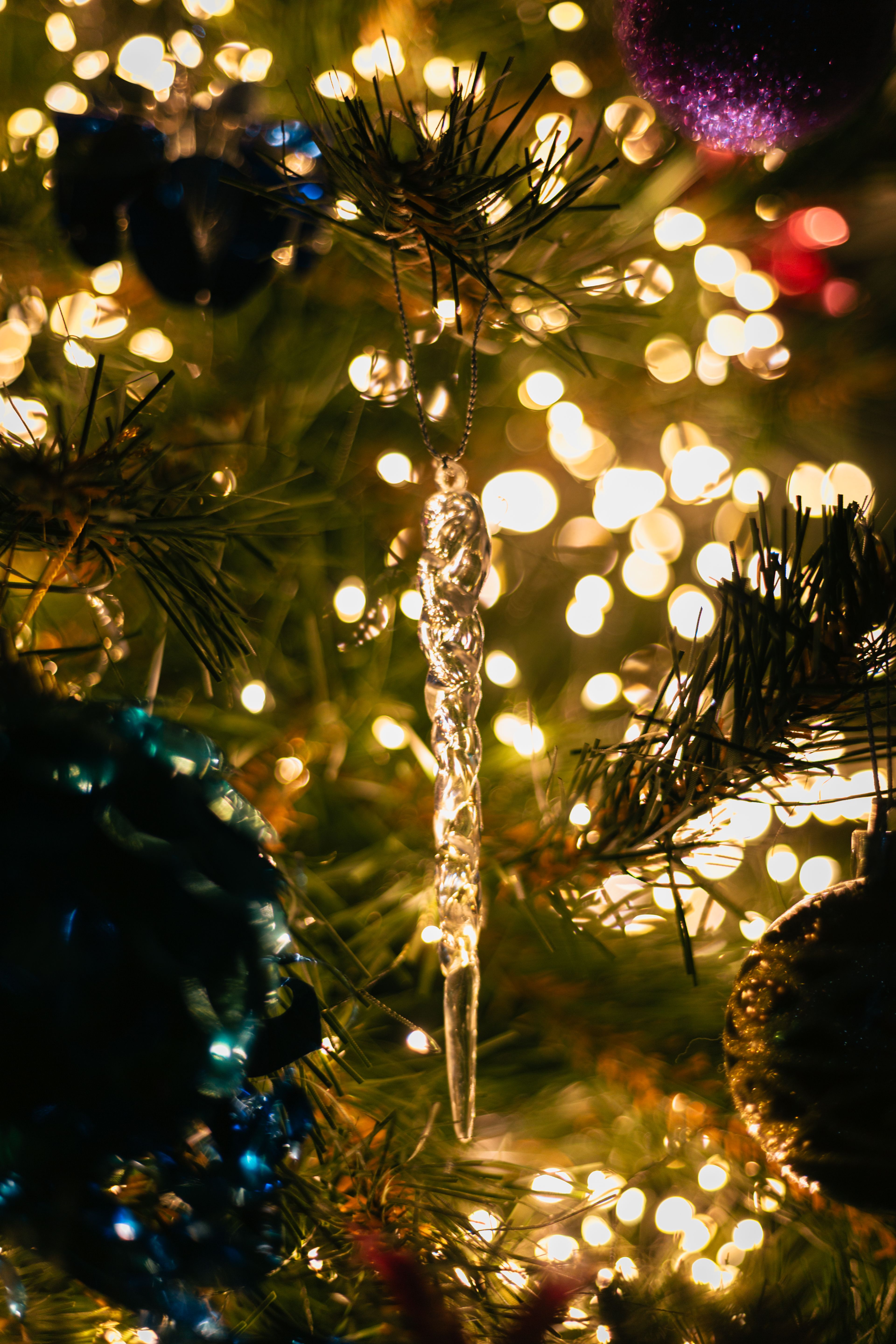 Close-up of a festive Christmas tree adorned with a sparkling icicle ornament amidst twinkling lights.