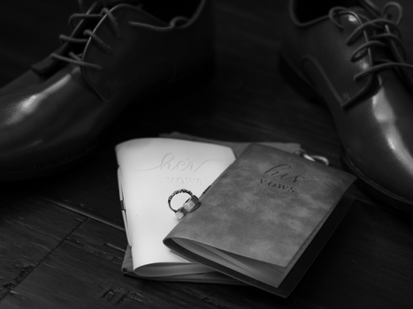 Black and white close-up of wedding vows booklets and ring, capturing elegance and love.