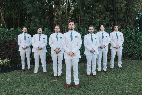 Free Seven groomsmen in white suits stand in a garden setting. Stock Photo