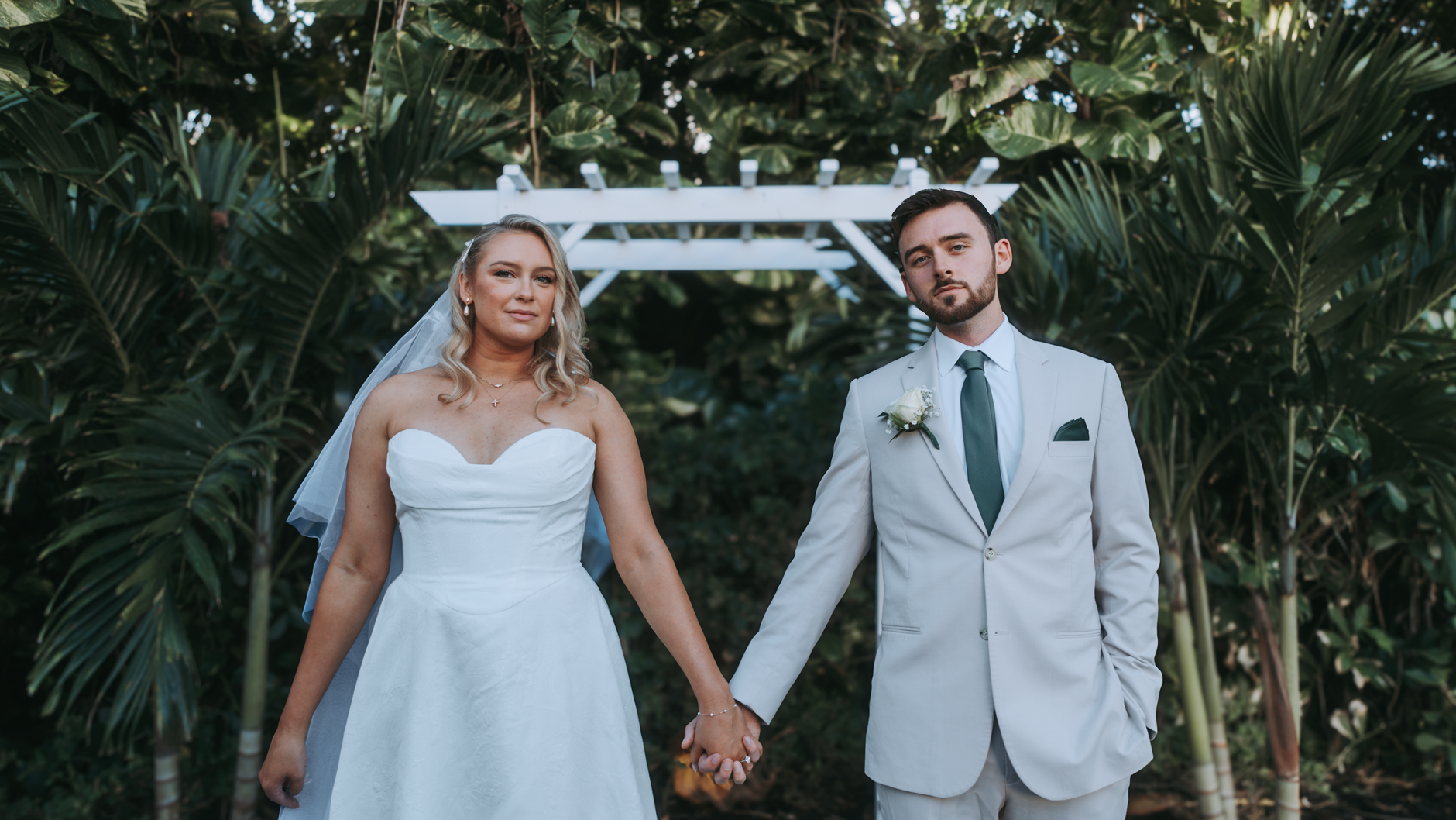 Komitmen Standar Pelayanan dan Dokumentasi Kualitas di Setiap Acara wedding Anda 3 A bride and groom holding hands under a white arch in an outdoor wedding setting.