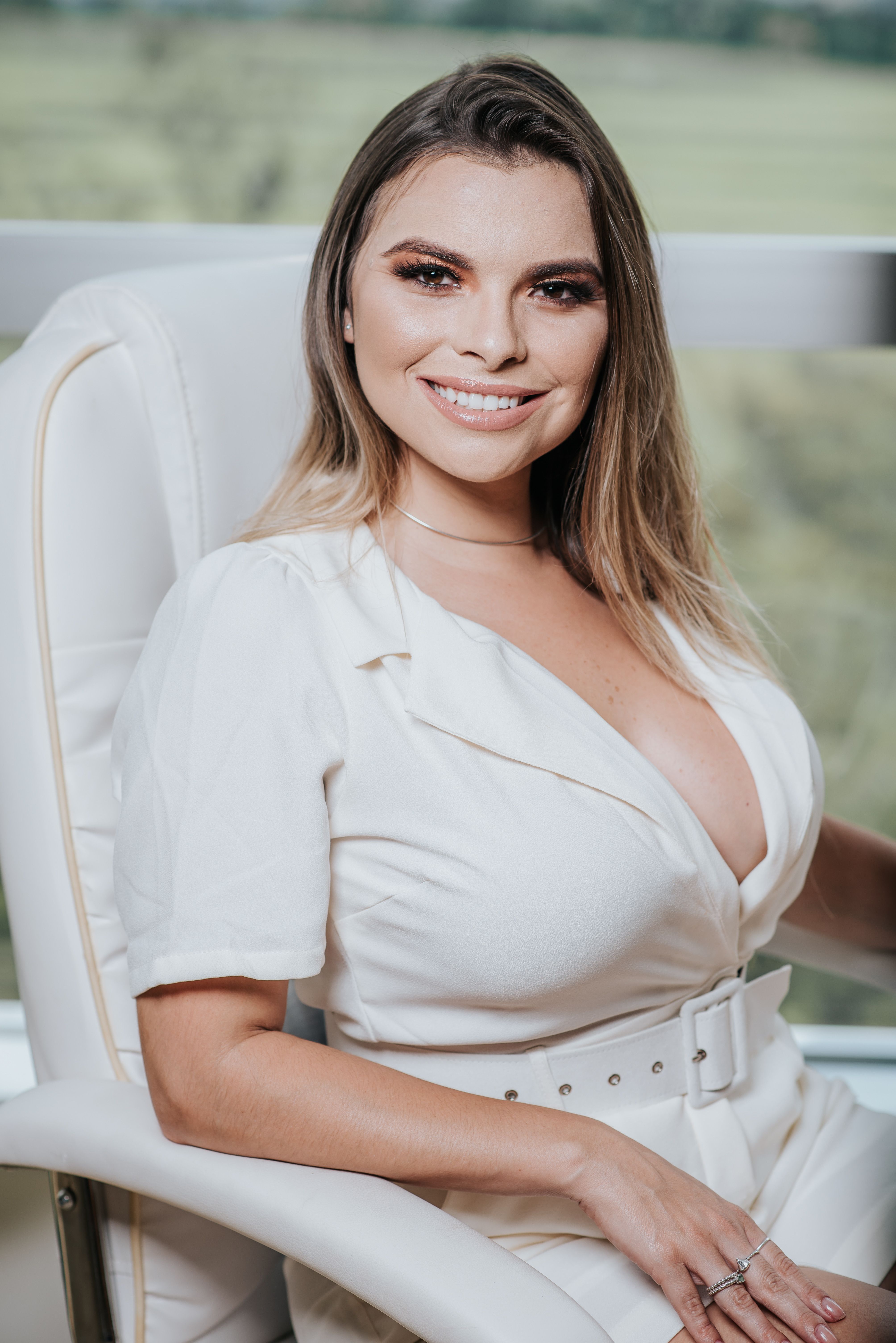 Charming woman with blonde hair smiling while seated comfortably indoors.