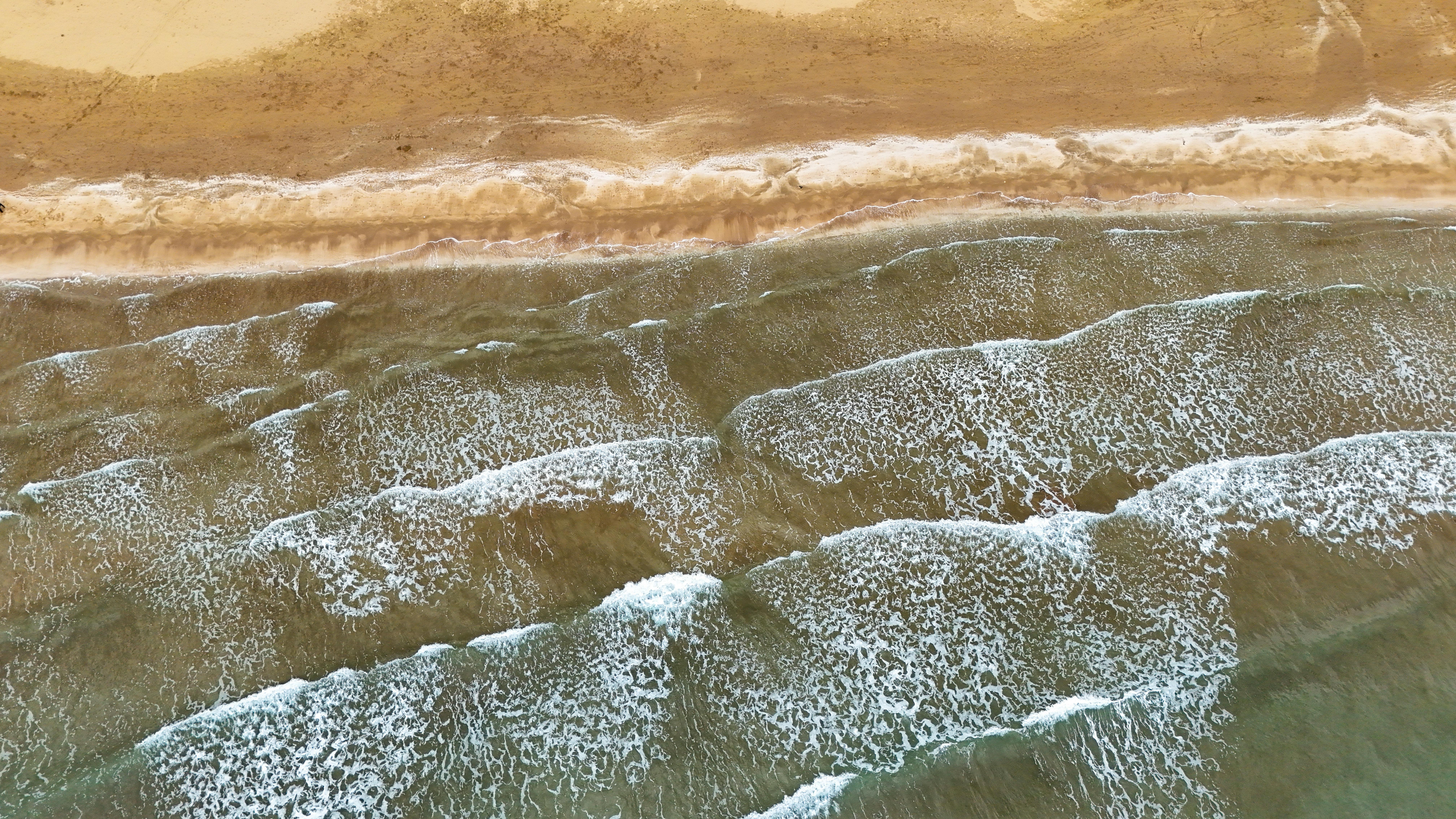 ingyenes Légi felvétel az óceán hullámairól, ahogy mintákat alkotnak a homokos tengerparton. Ideális relaxációs témákhoz. Stockfotó