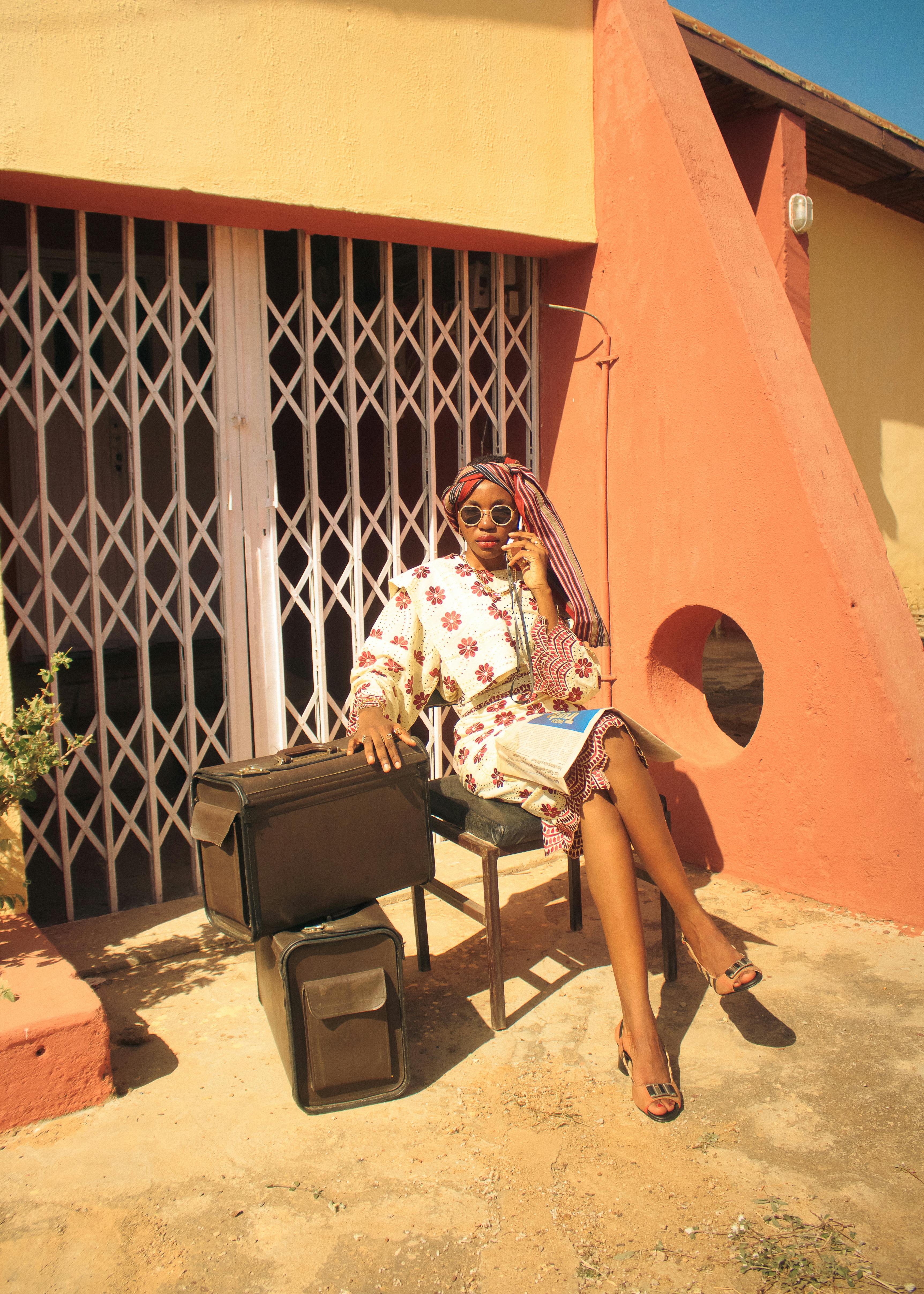 Free Chic woman seated outside with a vintage suitcase, exuding retro vibes and travel readiness. Stock Photo
