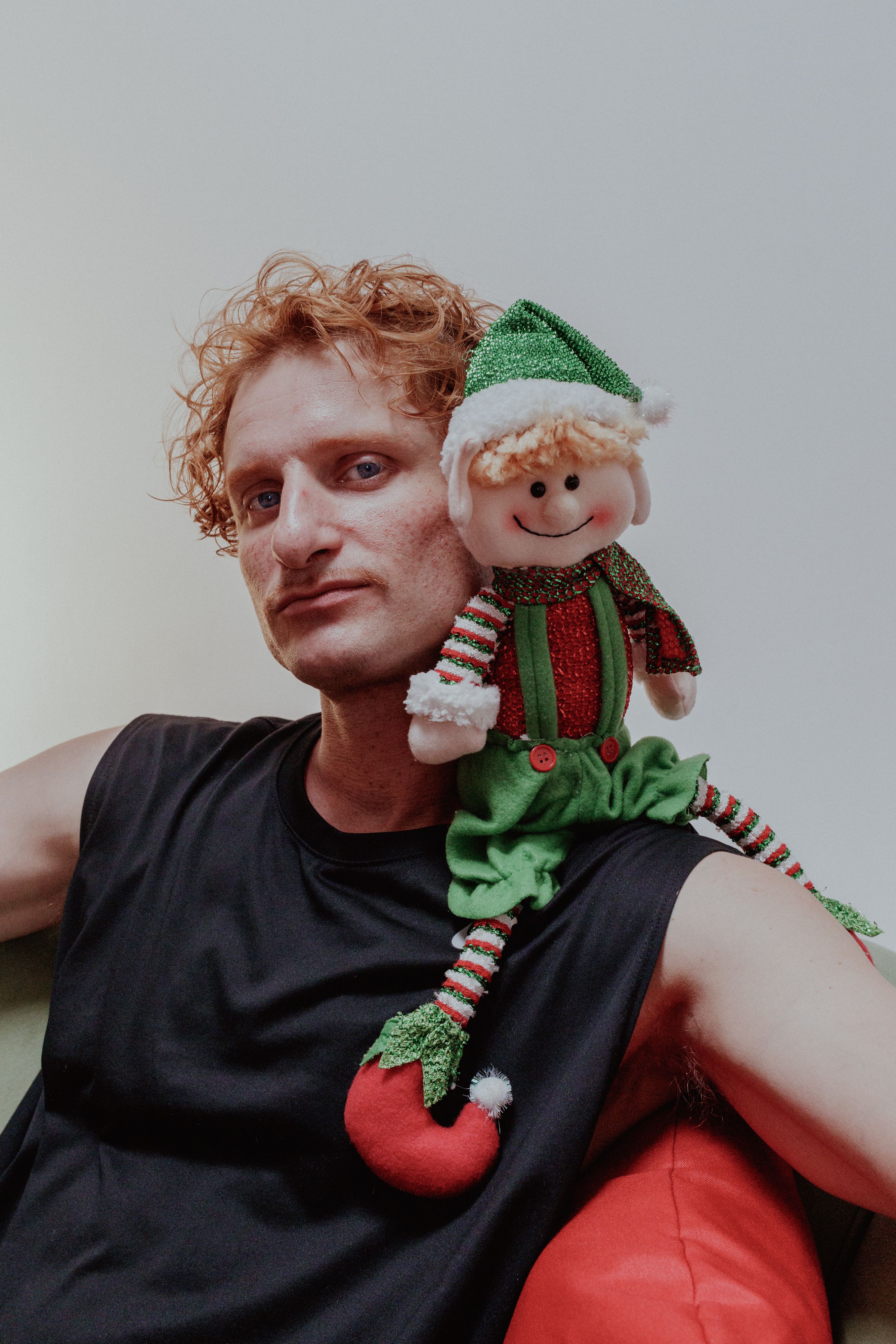 Man posing with a Christmas elf toy on his shoulder, celebrating the holiday spirit.