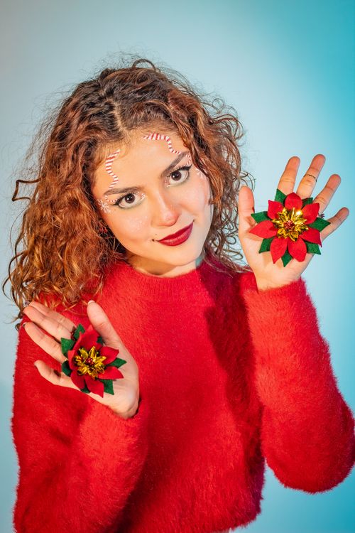 Free Young woman in red sweater holding festive poinsettias, embodying joyful holiday spirit, colorful background. Stock Photo