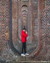 Free Man in Red Jacket and Black Pants Standing on Red Brick Wall Stock Photo