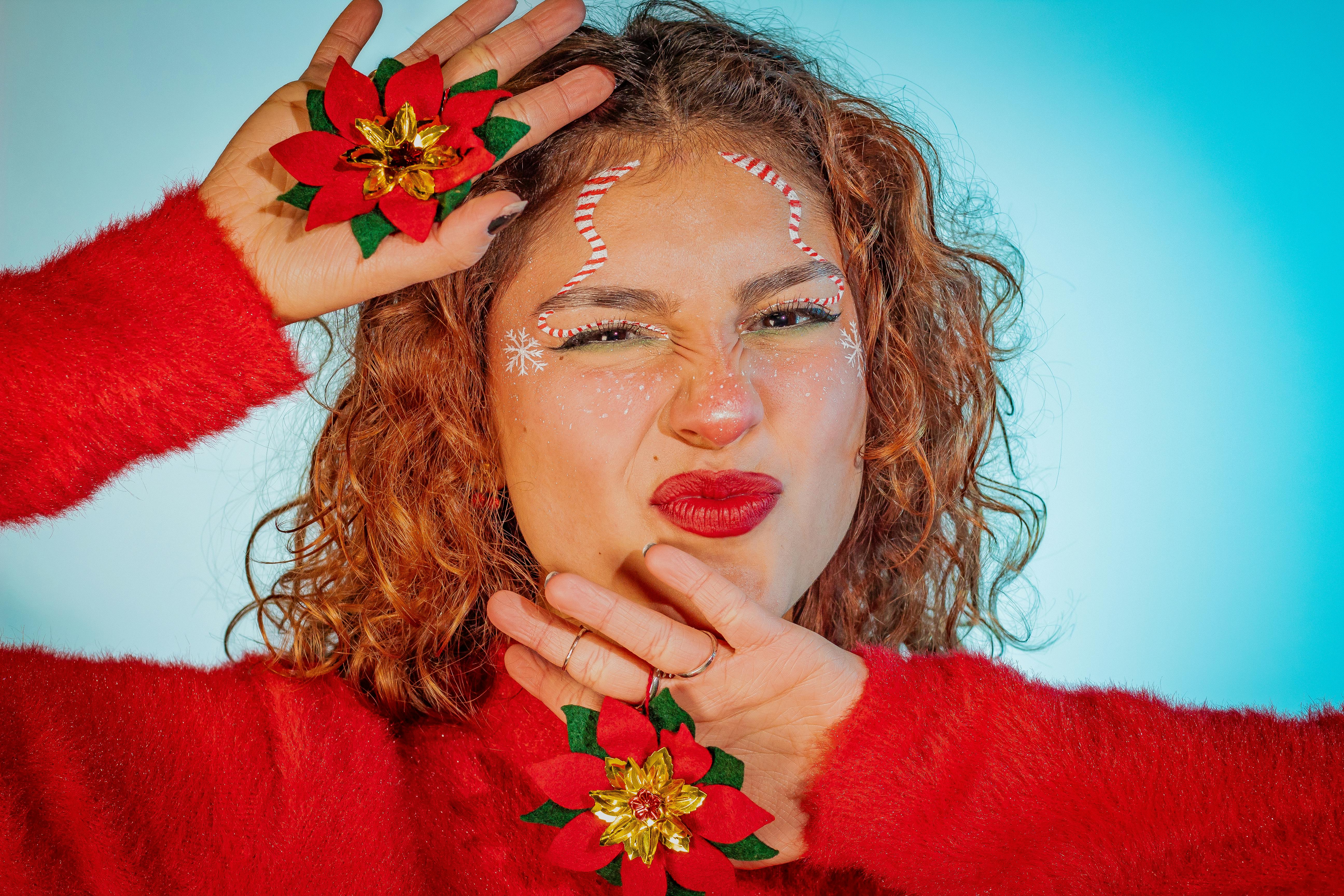 Cheerful woman in red sweater posing with festive poinsettia-themed makeup for the holiday season.