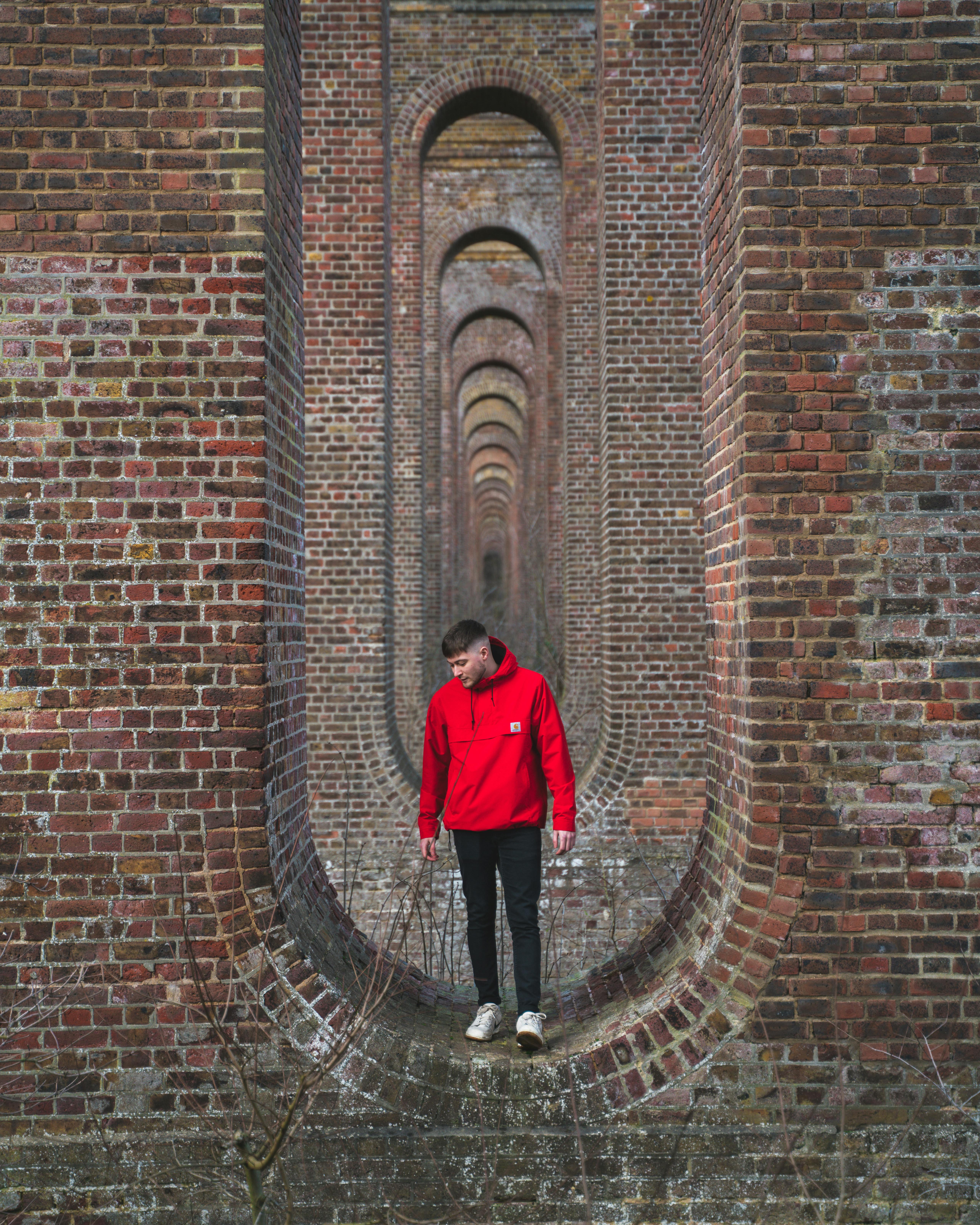 man in red jacket standing on brick wall