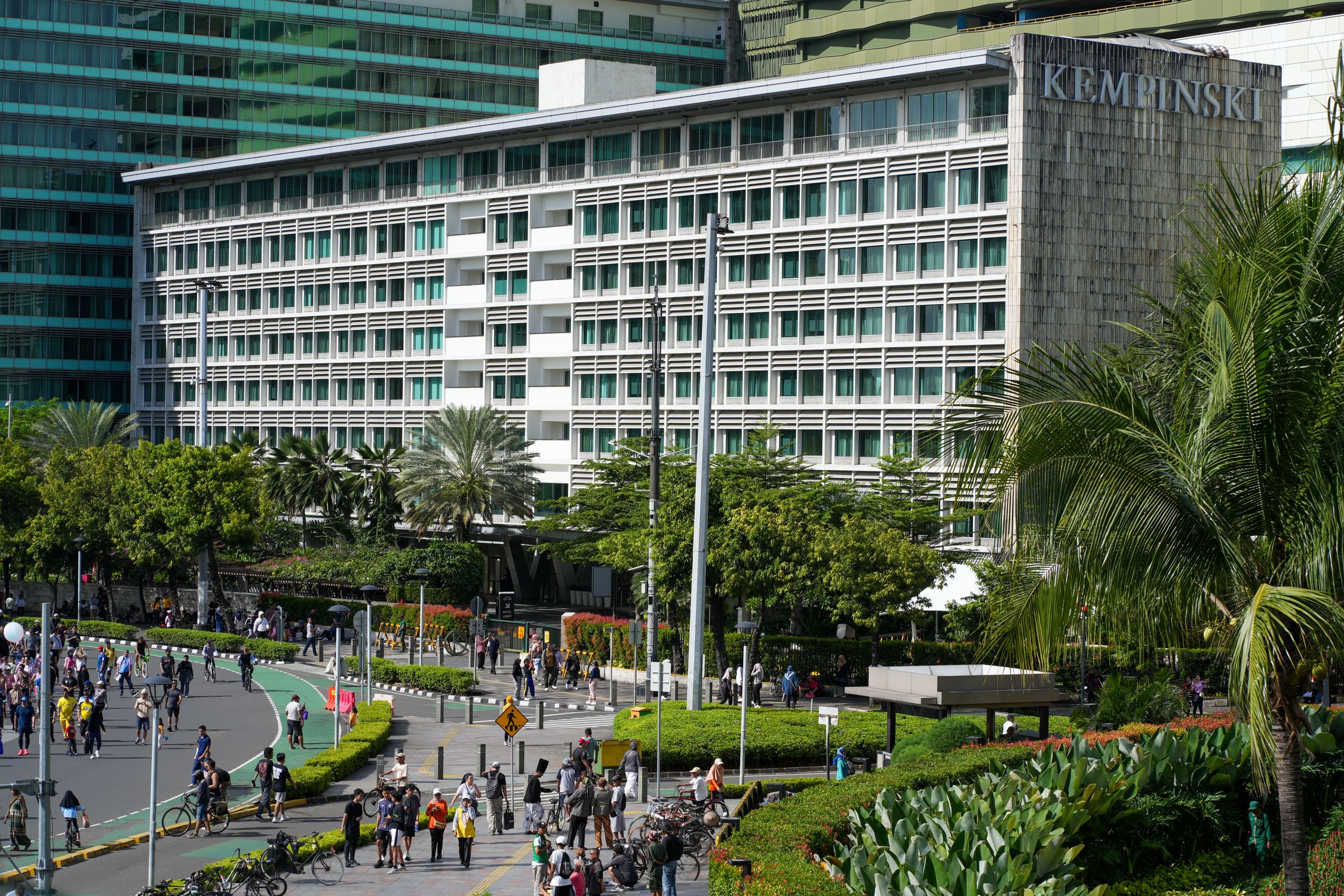 A vibrant view of the Kempinski Hotel in downtown Jakarta with people walking and cycling nearby.