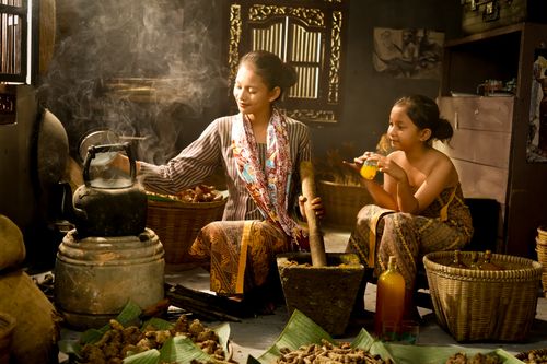 Free Indonesian mother and child in a traditional kitchen setting preparing herbs and drinks. Stock Photo