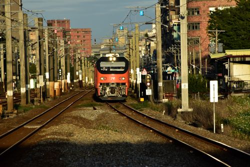 Free A red commuter train approaches on urban railway tracks under a bright sky. Stock Photo