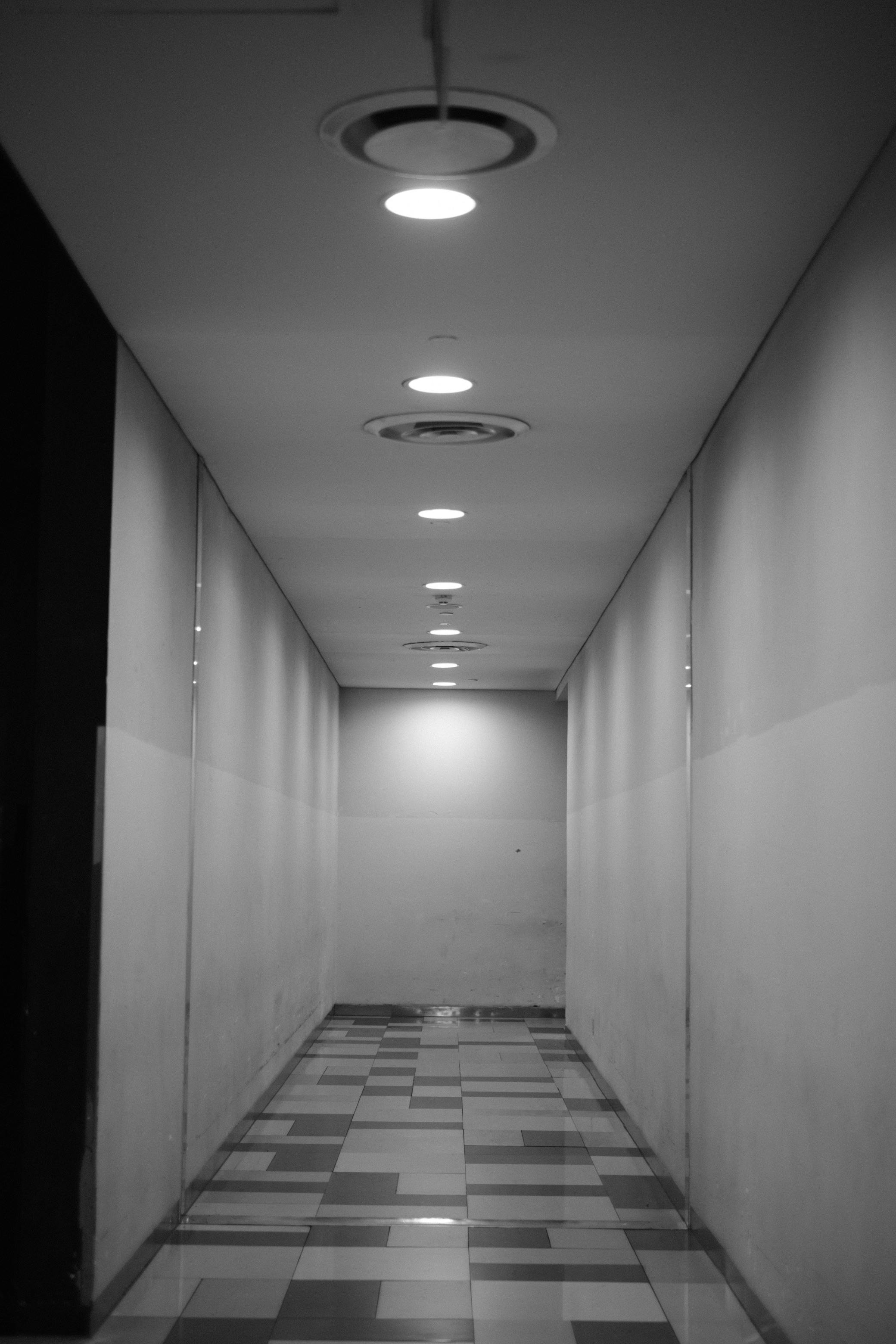 Gratis Lorong minimalis hitam putih dengan lampu langit-langit yang menciptakan suasana yang temaram. Foto Stok