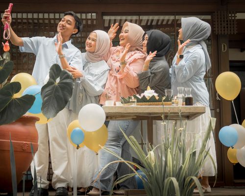 Free A joyful group of five friends taking a selfie together outdoors with balloons, plants, and festive decor. Stock Photo