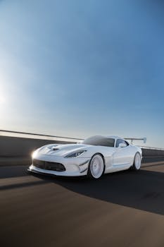 White sports car speeding down highway under clear blue sky at sunrise.