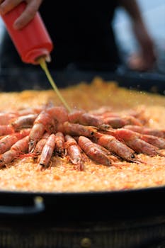 Close-up of traditional seafood paella with shrimp being drizzled with oil.