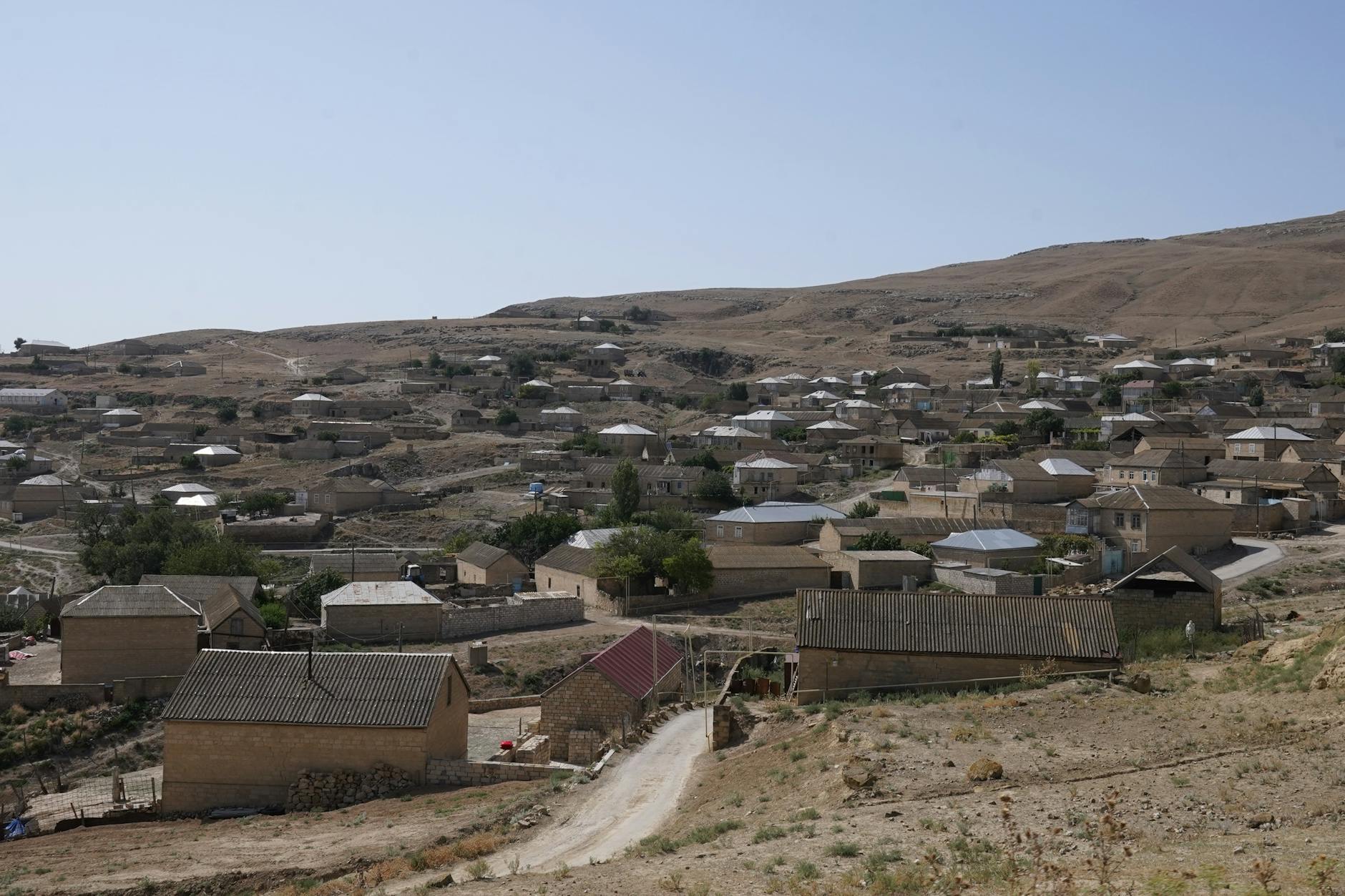 Scenic view of a rural village in a dry, hilly landscape under a clear sky.