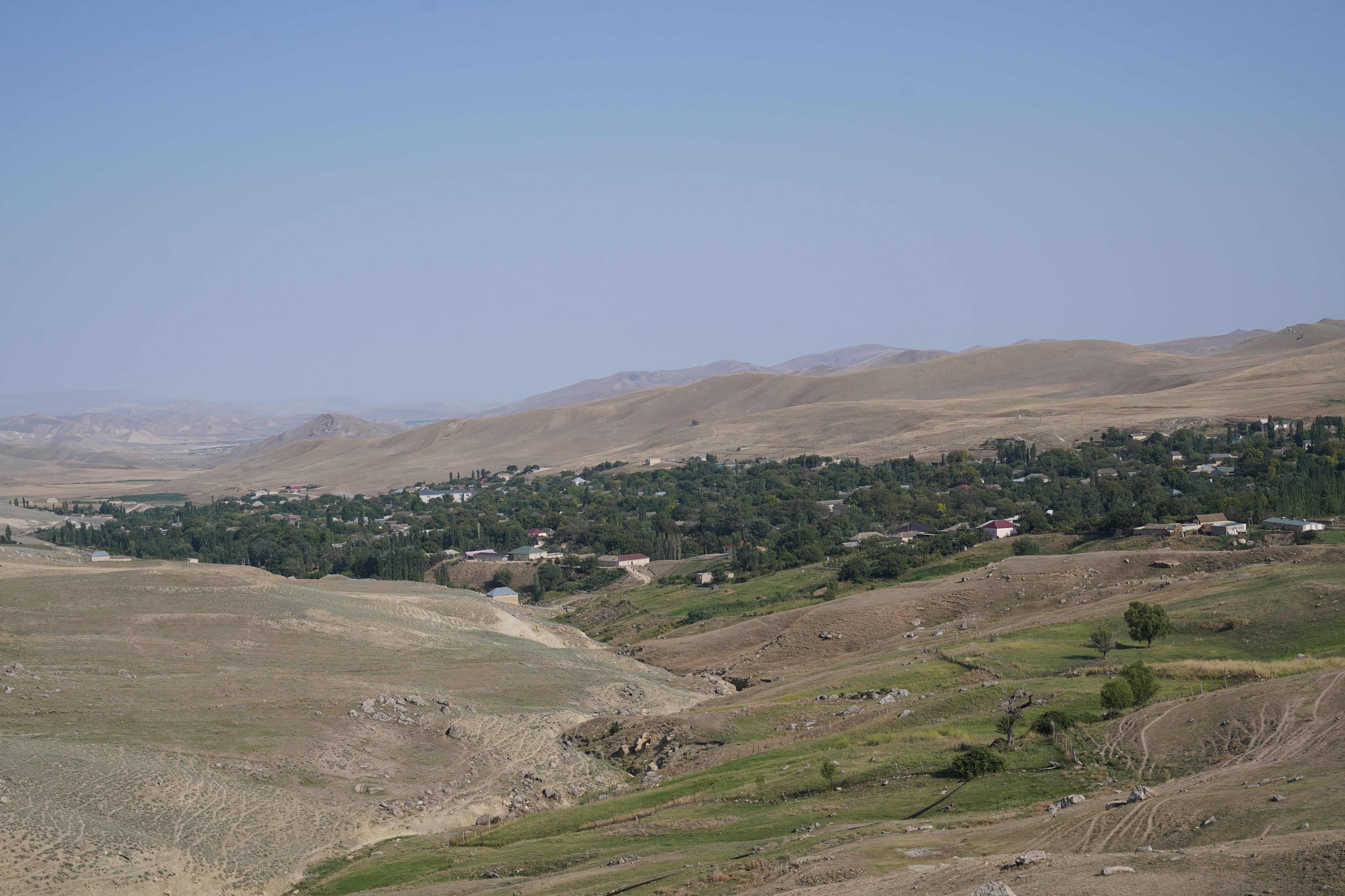 Expansive rural landscape with village nestled among hills under a blue sky.
