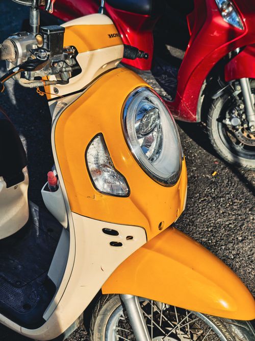 Free Close-up of yellow and red vintage scooters parked outdoors on a sunny day. Stock Photo