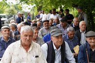Senior men gathered outdoors, engaging in social interaction under trees.
