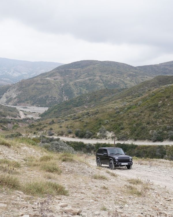 Black SUV navigating rugged mountain terrain under overcast skies.