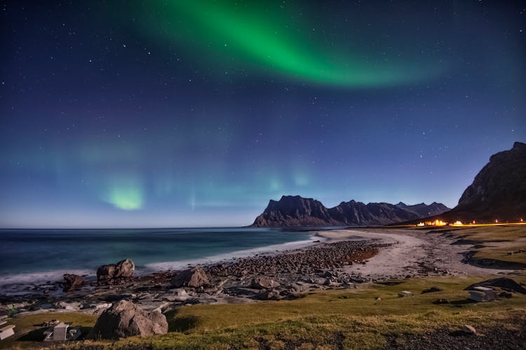 Body Of Water Near Mountain Under Green Sky