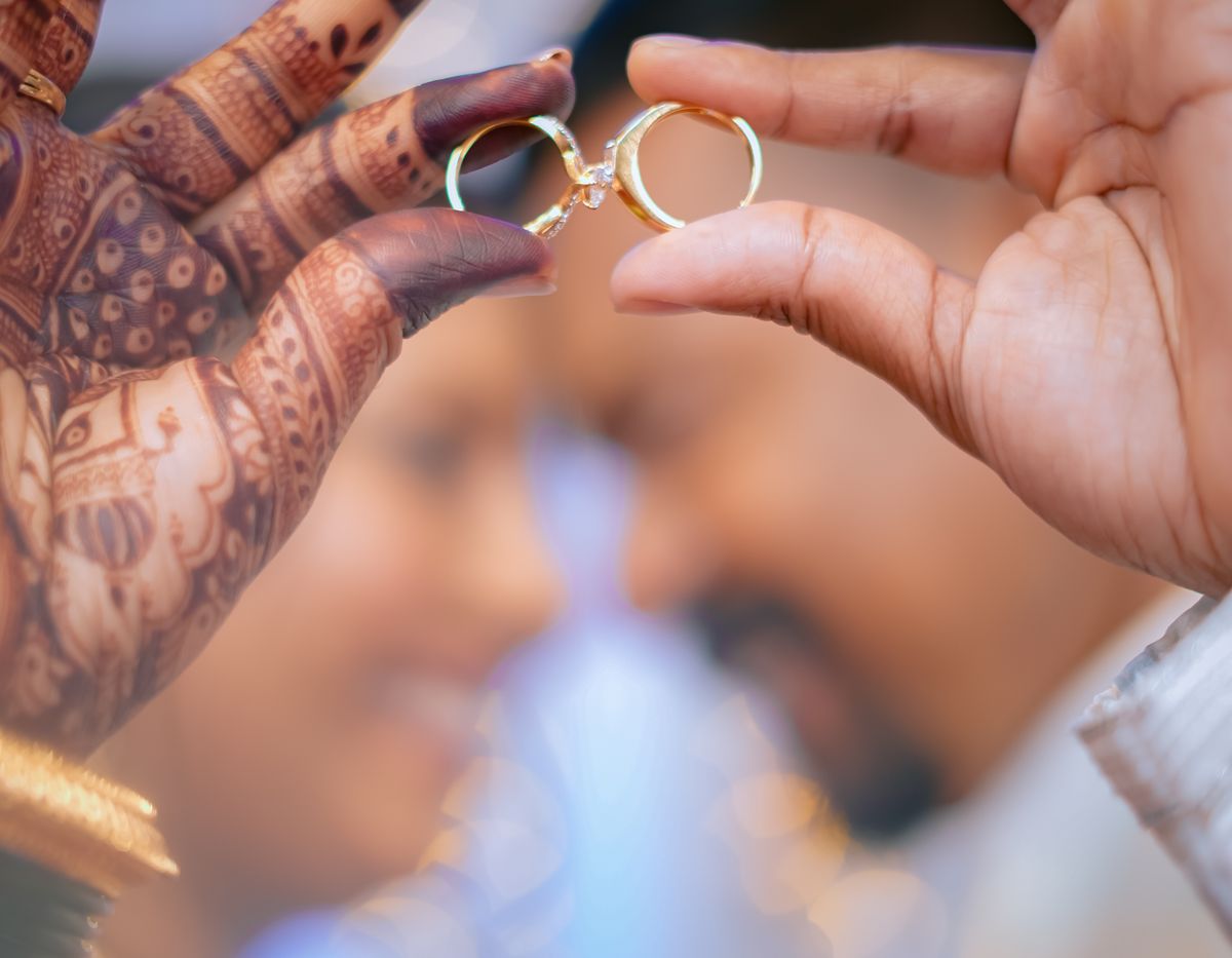 Couple holding rings, hands decorated with henna