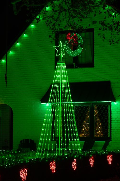 Free Bright green and red Christmas lights adorn a house at night, featuring a lit tree and wreath. Stock Photo