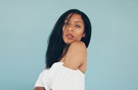 一位时尚的年轻女子身着白衣，在蓝色背景前优雅地摆着姿势