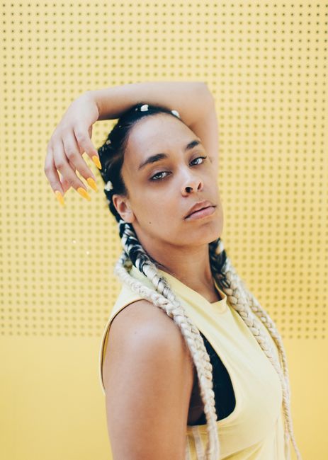 Woman with braided hair poses gracefully against a vibrant yellow backdrop.