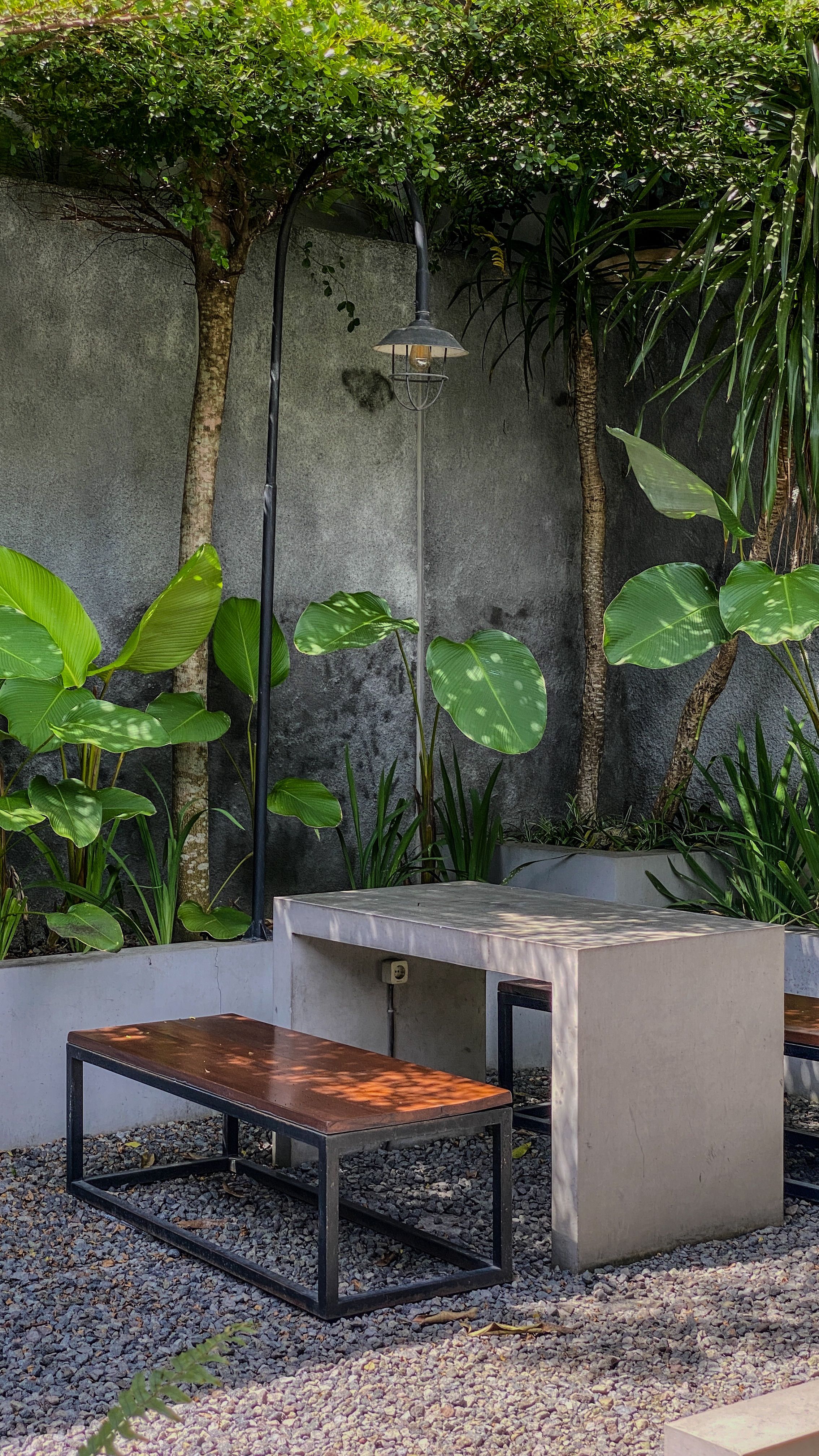 Small concrete bird bath sitting on a bed of smooth river rock and pea gravel on a patio edge