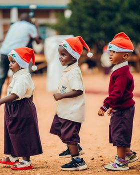 Three children wearing Santa hats celebrate Christmas outdoors. Festive mood, joyful occasion.