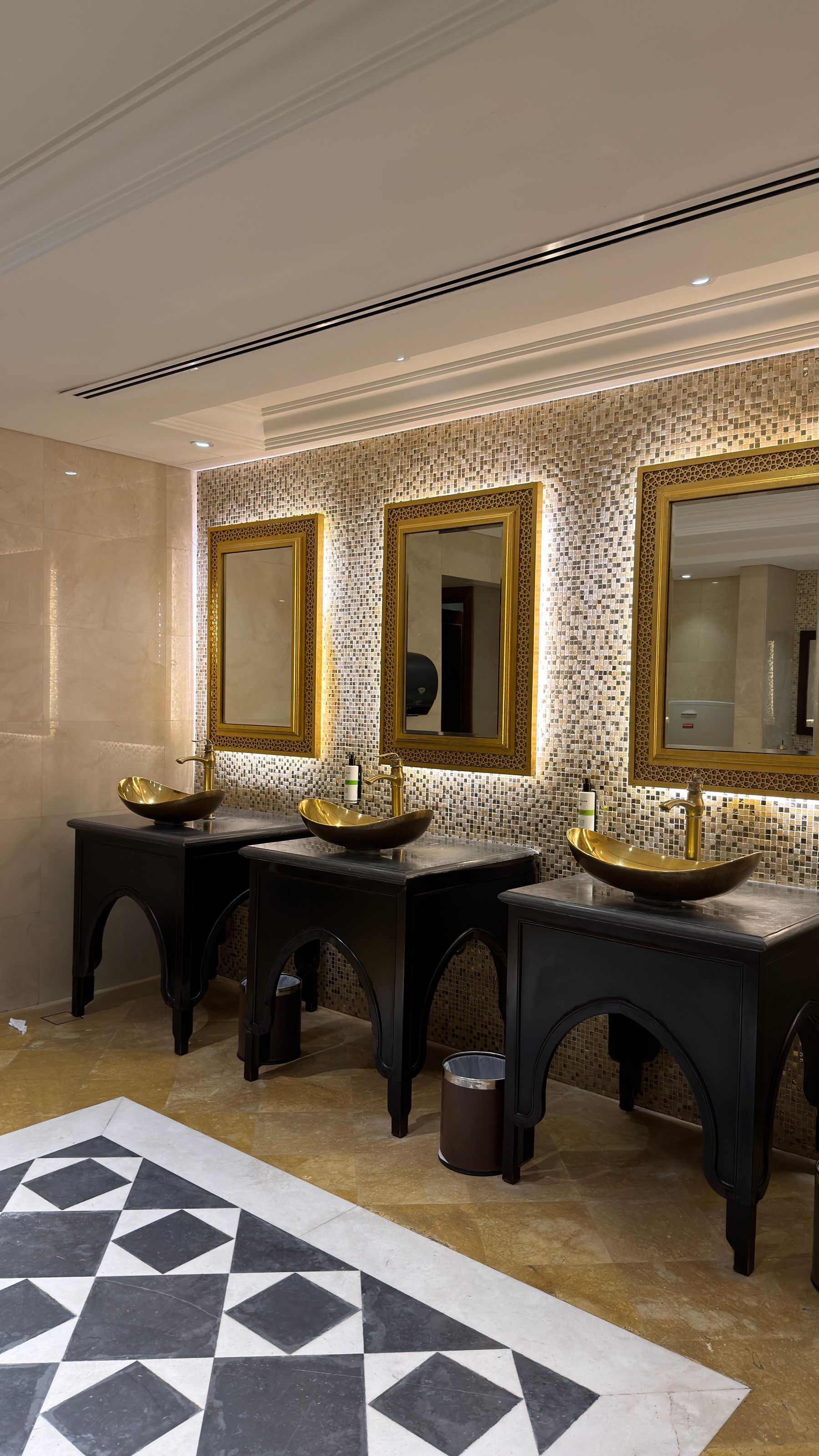 Elegant bathroom with black sinks, gold-framed mirrors and patterned flooring