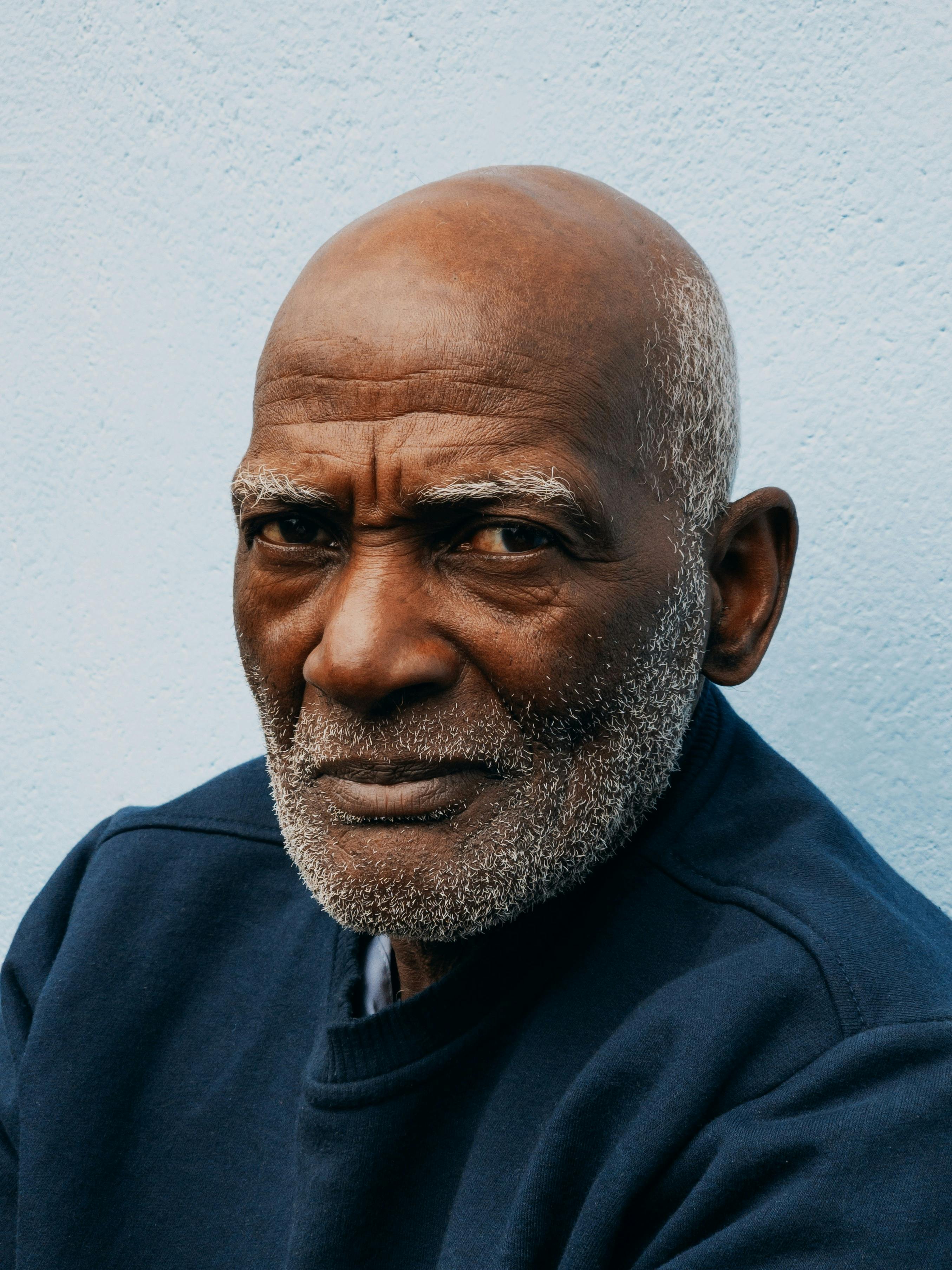 Gratis Nærbilde av en eldre mann med et ettertenksomt blikk mot en lyseblå bakgrunn. Arkivbilde