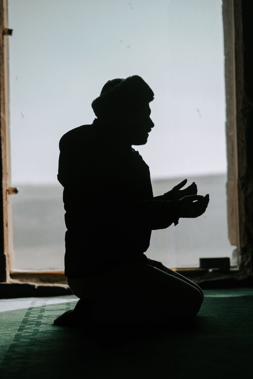 Free A silhouette of an individual praying indoors with sunlight streaming in through a window. Stock Photo