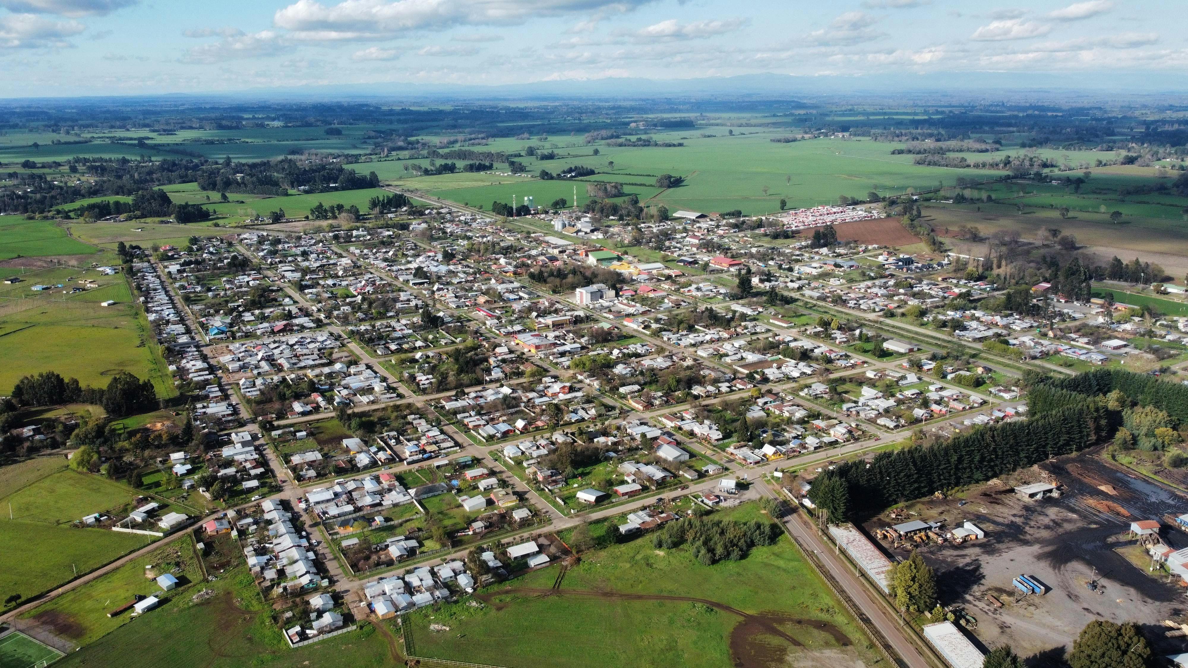 Aerial photo of a rural town surrounded by green fields under a cloudy sky, showcasing its layout.