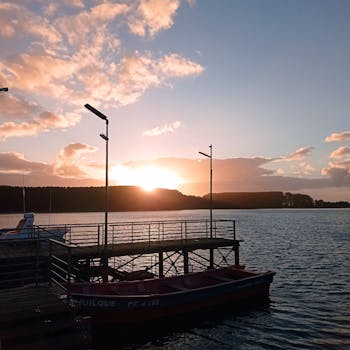 Tranquil sunrise view over a lakeside dock with boats and serene water reflections.