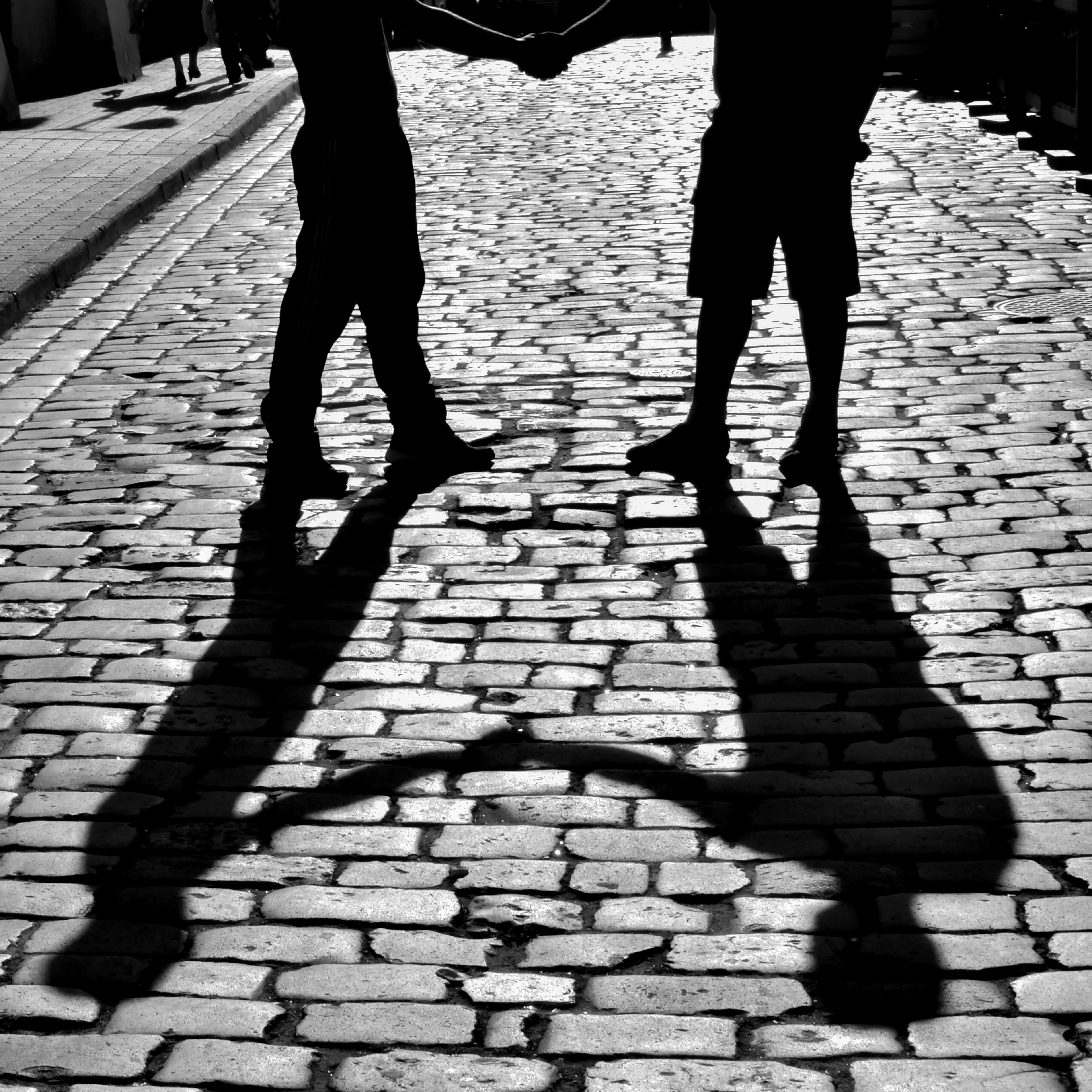 Silhouette of two people shaking hands, casting shadows on a cobblestone street in Rzeszów, Poland.