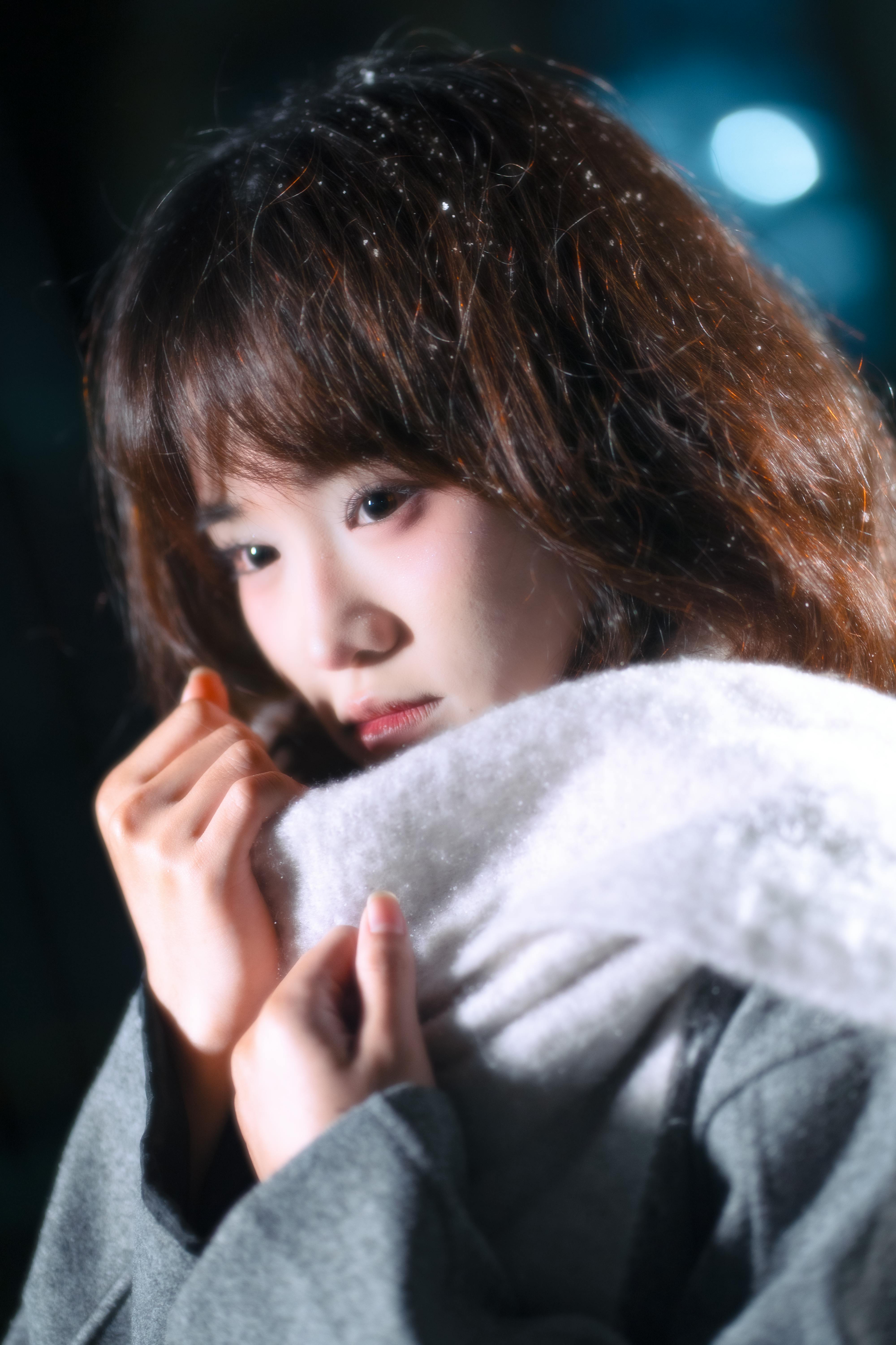 Close-up portrait of a young woman in winter clothing against a moody evening backdrop.