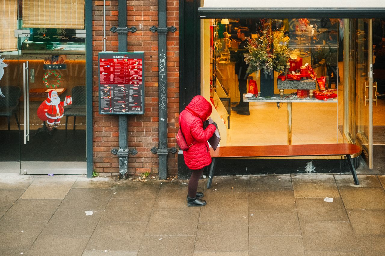 woman in red coat window shopping at a decorated store during the holi