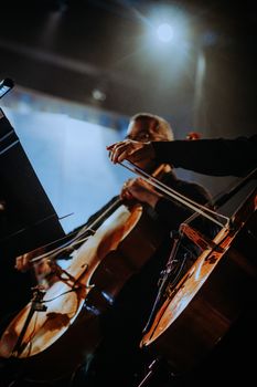 A cellist passionately plays during an orchestral concert under dramatic lighting.
