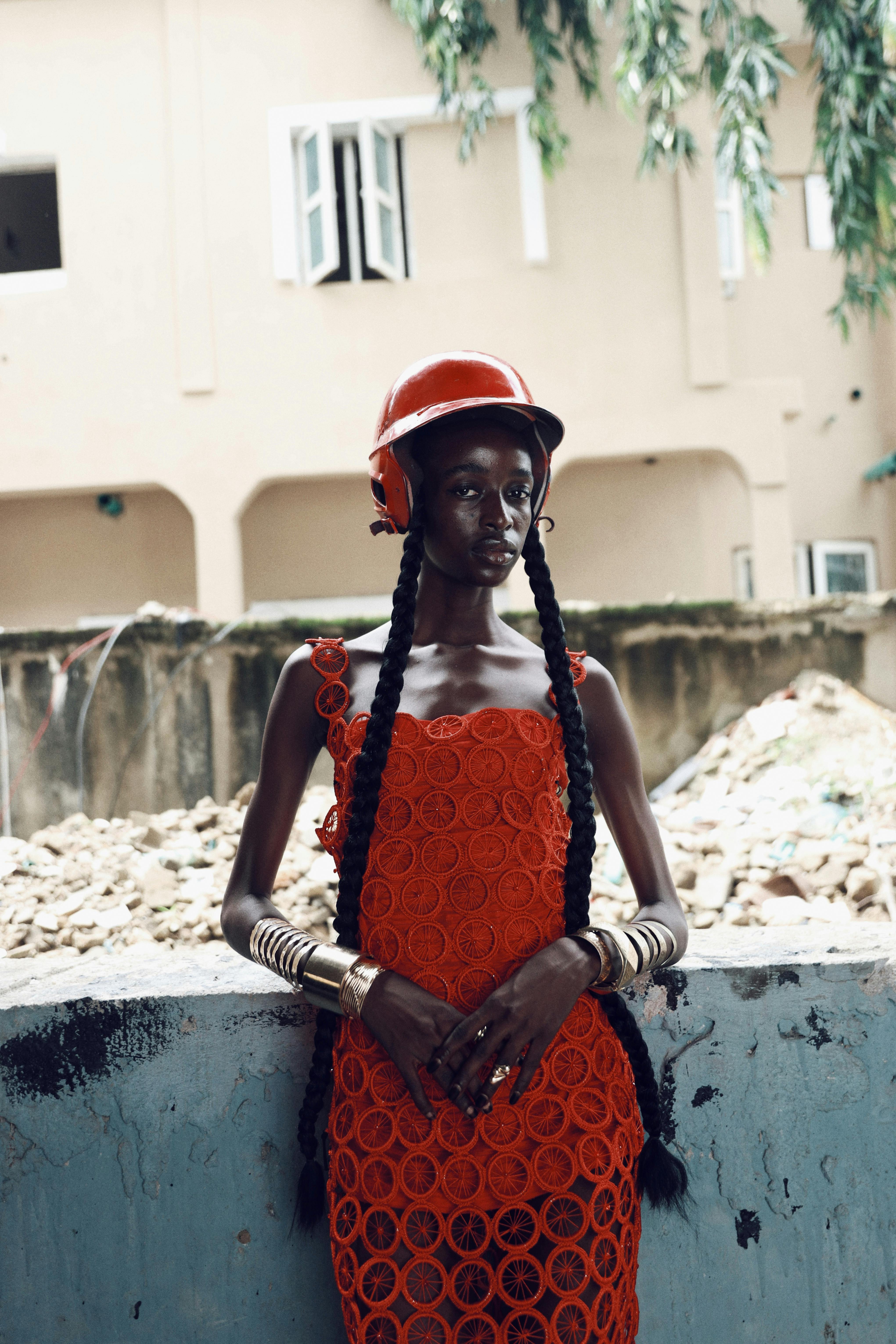 Stylish woman stands confidently wearing red dress and hard hat at a construction site in Accra, Ghana.