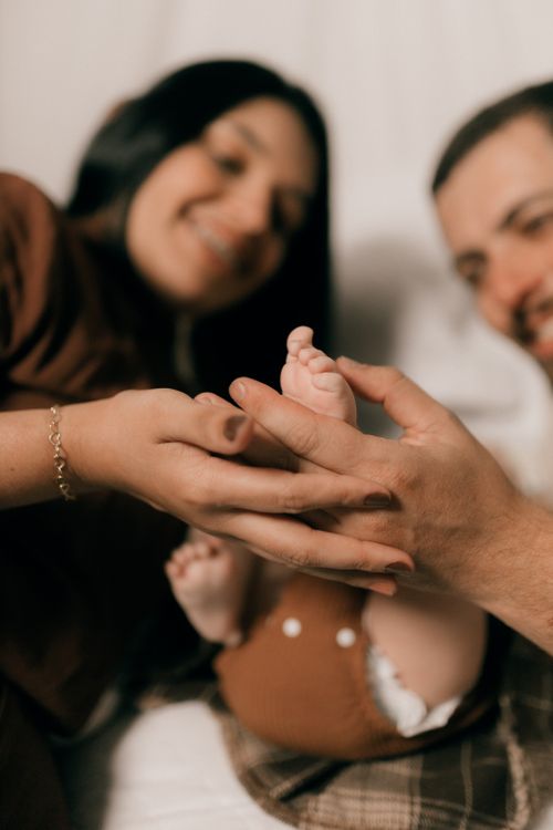 Free Close-up of smiling parents gently holding their newborn baby's feet, showcasing love and connection. Stock Photo