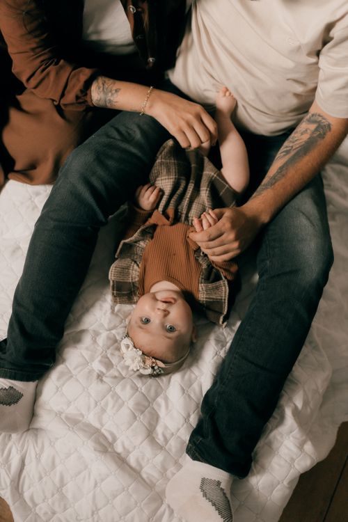 Free Overhead view of a smiling baby between parents on a cozy bed. Stock Photo