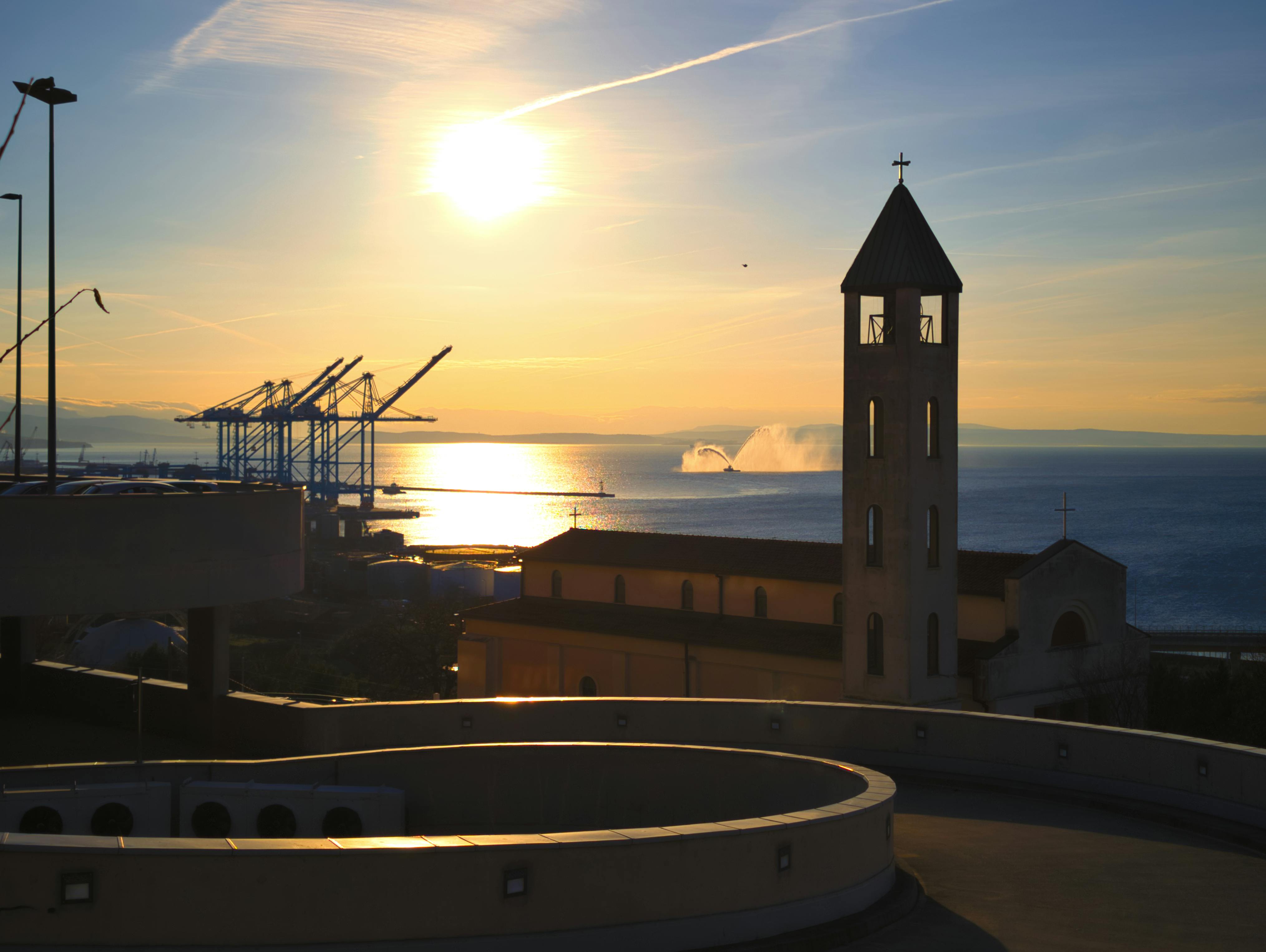 Peaceful sunset over Rijeka port, with church tower silhouetted against the sea.