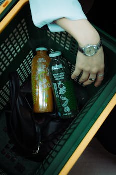 A hand reaches into a shopping basket with bottled drinks and a bag, capturing a candid shopping moment.