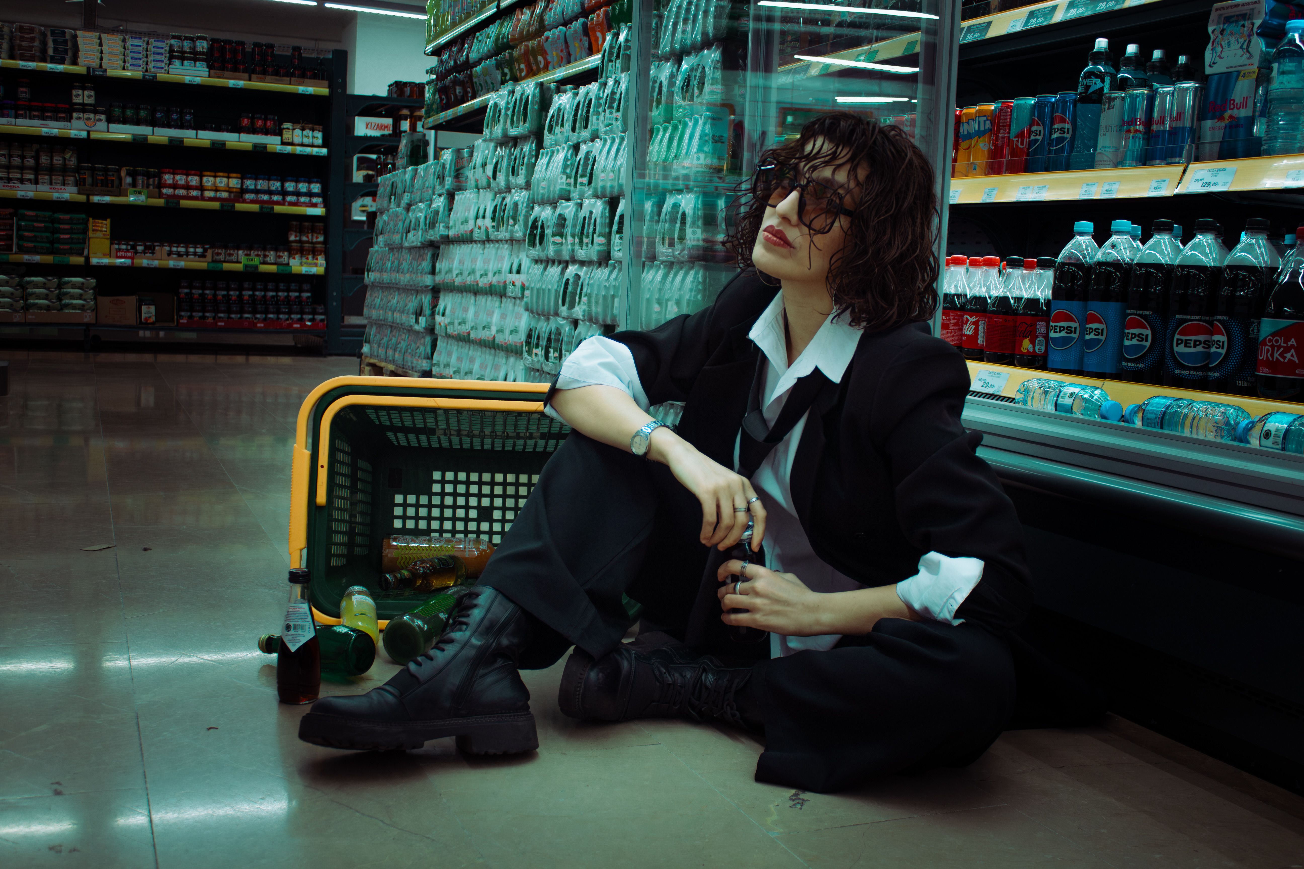 Stylish woman in suit sitting on a supermarket floor, with a shopping cart.