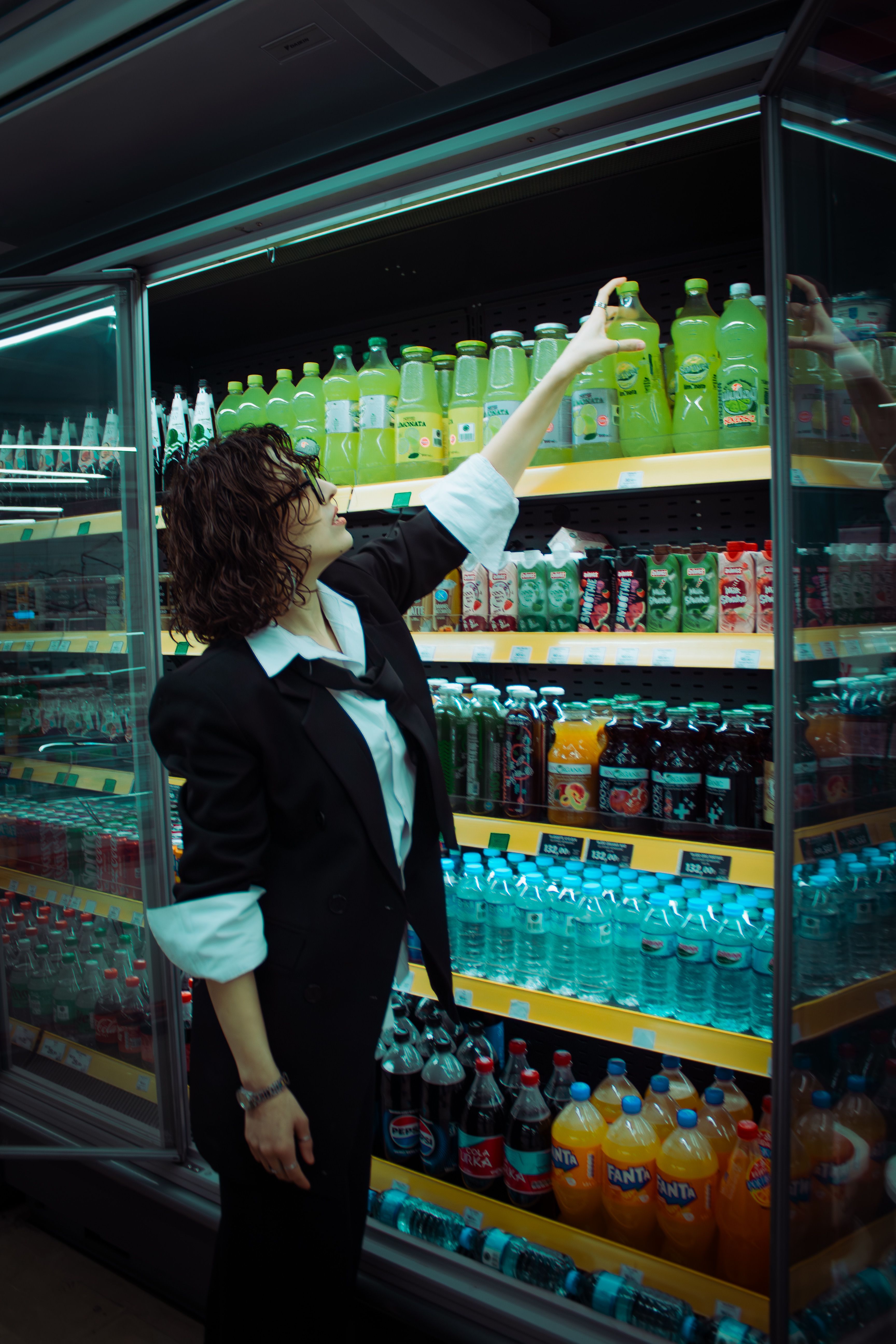 A woman in a black jacket reaches for a drink in a supermarket beverage aisle.