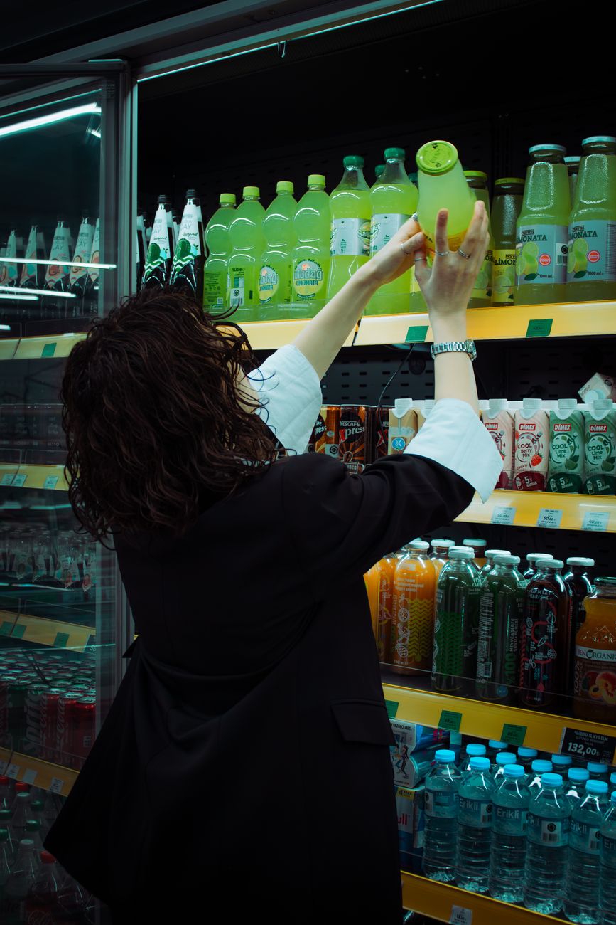 Mulher pega uma bebida verde no corredor do supermercado. Momento de compras movimentado.