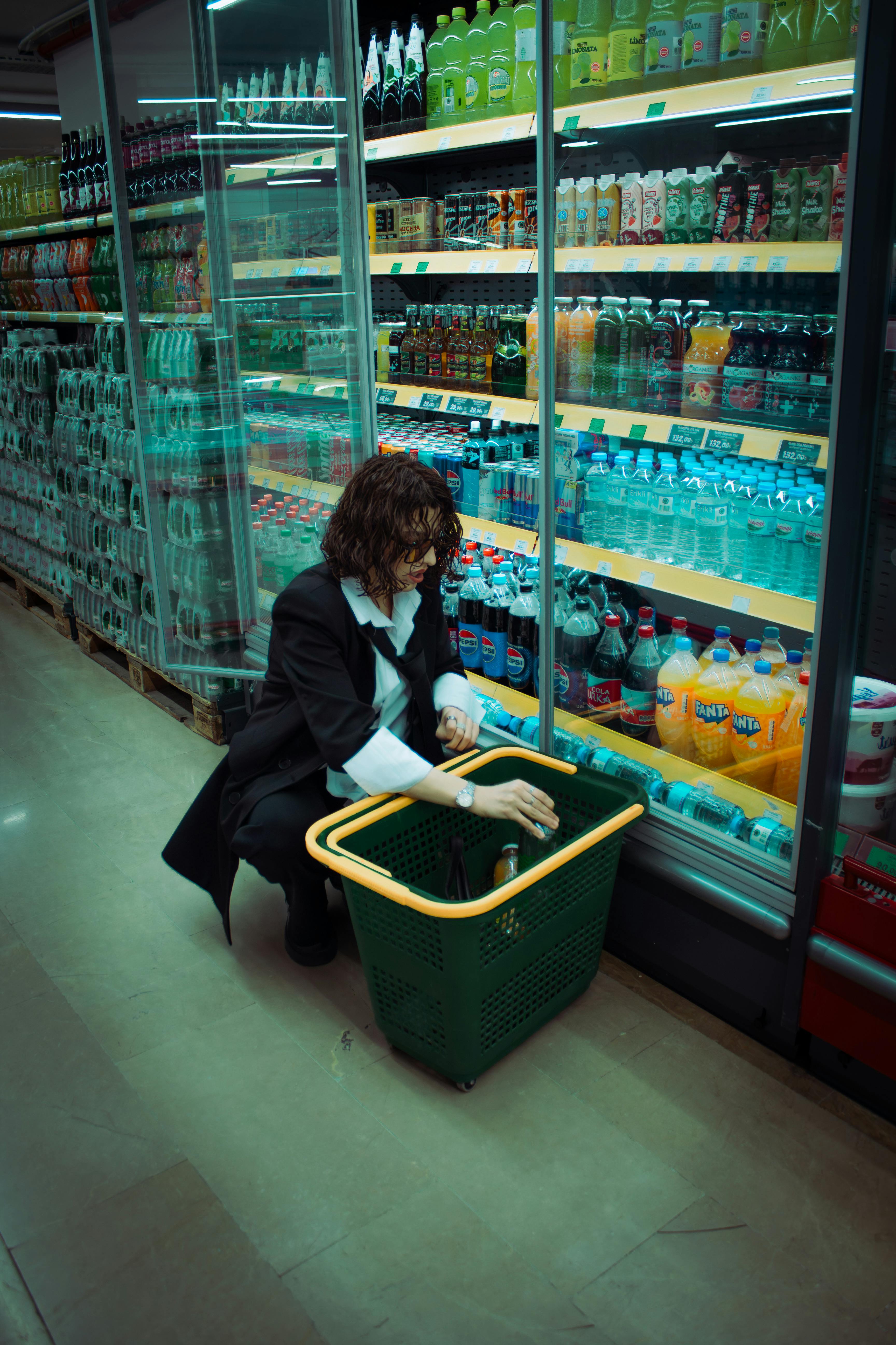 A woman in black suit shops in a grocery store's beverage aisle, filling a basket.