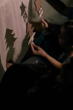 Kids crafting shadow puppets, projected on a white screen, evoking creativity.